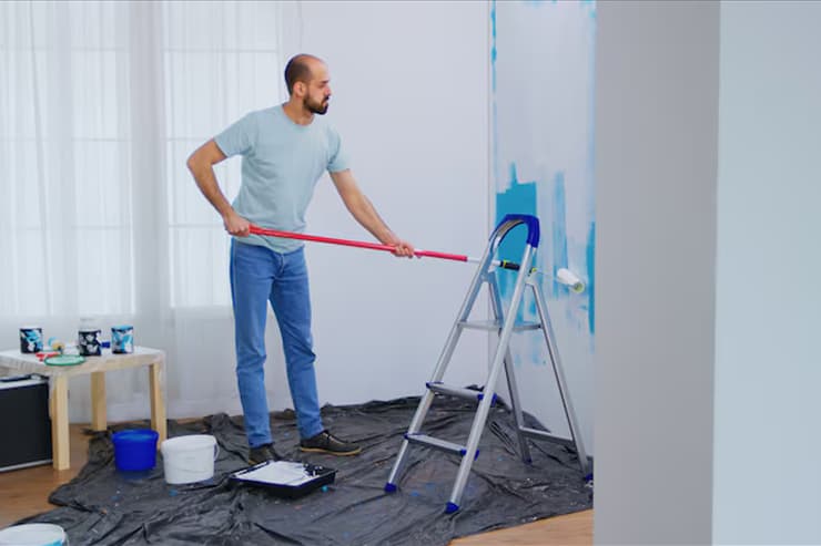 A man using a ladder to paint a room, showcasing a commercial painting project in progress.