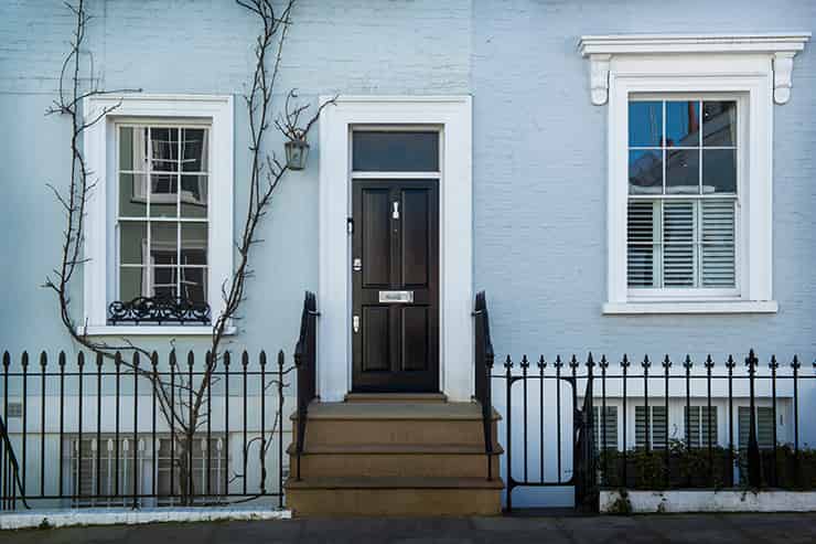 A blue house with white trim and a black door, depicted in a brick painting aesthetic.
