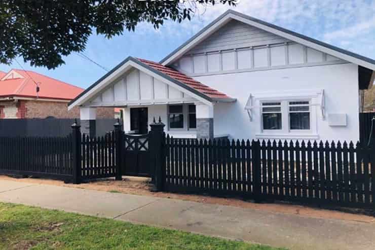 A render painting of a small white house surrounded by a black fence.