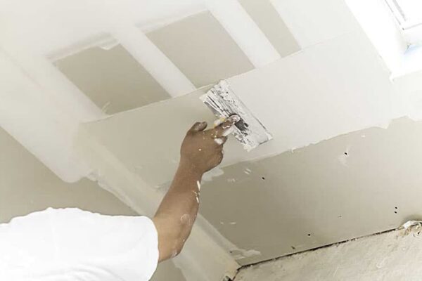 A man is fitting a light fixture in a room as part of a rental property repainting effort.