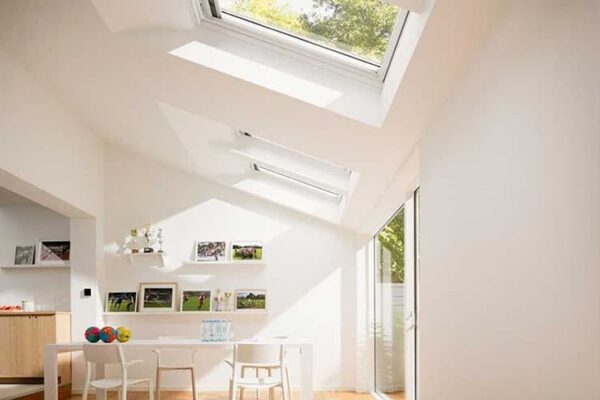 A spacious white room with natural light from skylights and a central table, highlighting a contemporary residential design.