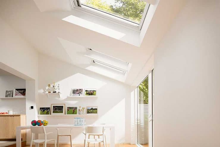 A spacious white room with natural light from skylights and a central table, highlighting a contemporary residential design.